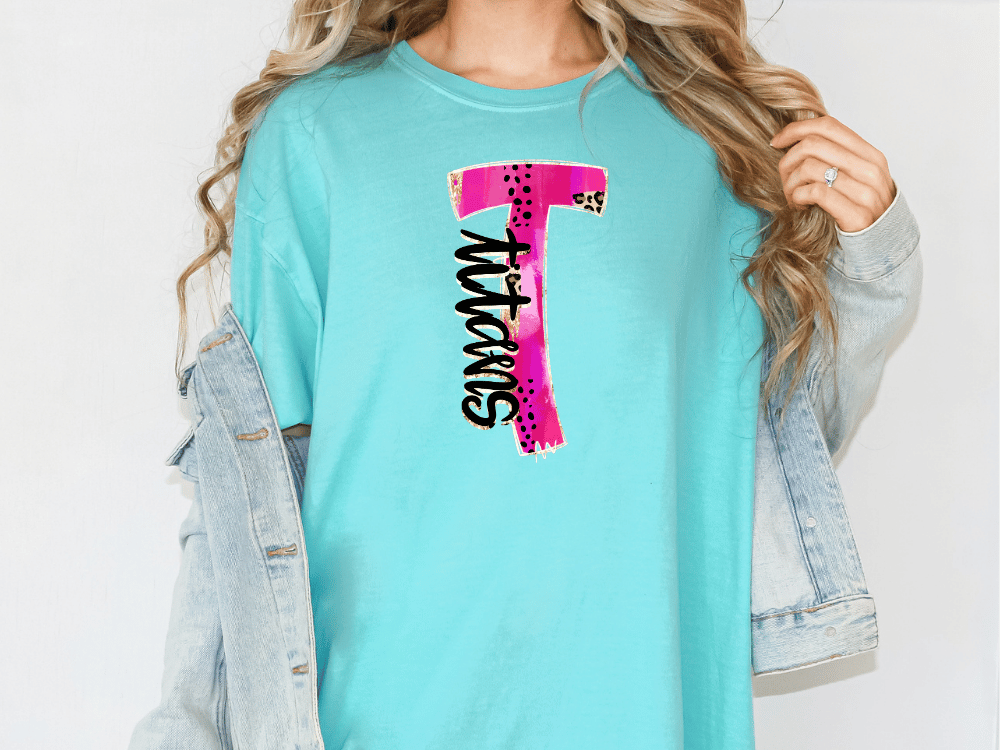 A woman wearing a turquoise t-shirt with a pink and black graphic design on it, and a denim jacket.