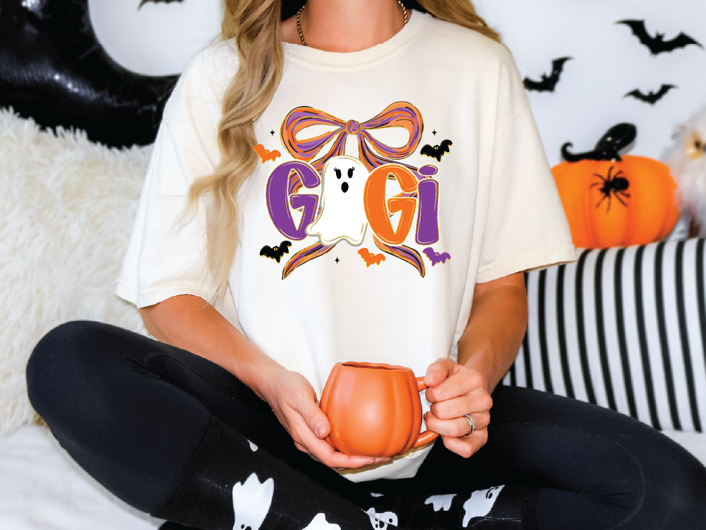 A woman wearing a white t-shirt with a Halloween-themed design is sitting on a couch, holding a pumpkin-shaped mug.