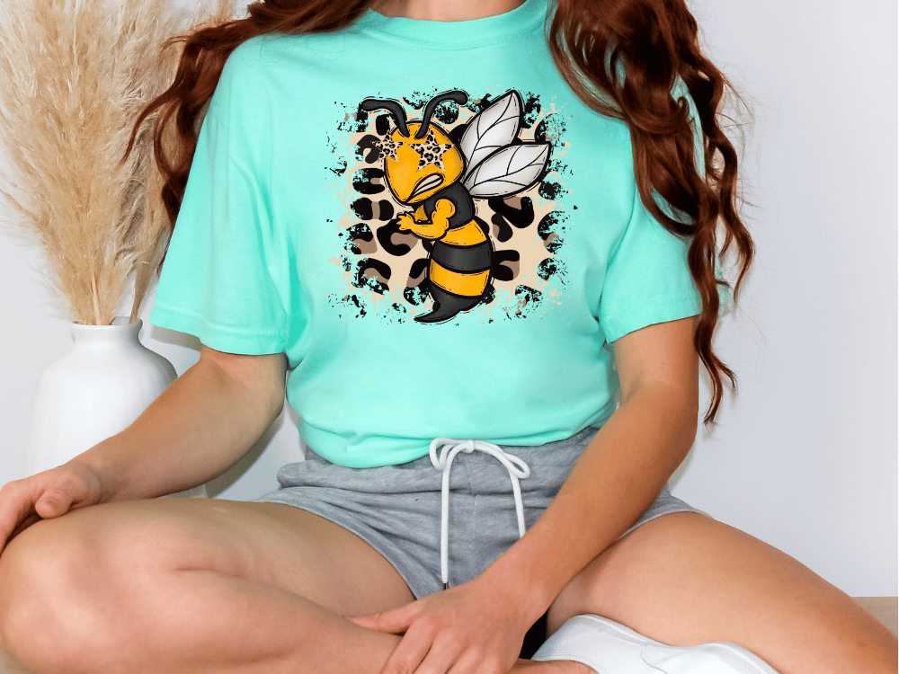 A person wearing a turquoise t-shirt with a cartoon bee graphic and grey shorts is sitting on the floor.
