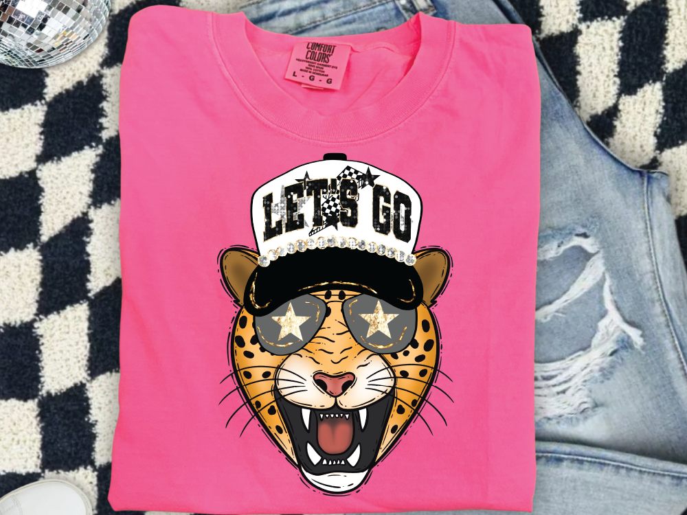 A pink t-shirt with a graphic of a smiling leopard wearing sunglasses and a baseball cap, along with the text "LET'S GO".