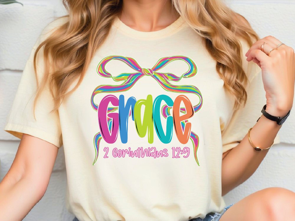 A woman wearing a white t-shirt with a colorful graphic design featuring the word "Grace" and a ribbon.
