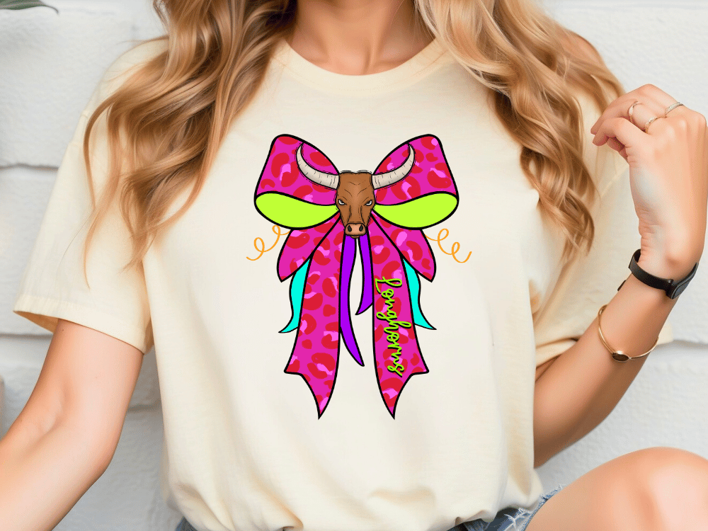 A woman wearing a white t-shirt with a colorful graphic design of a bull's head and a pink bow on it.