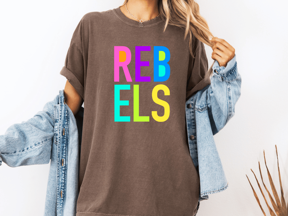 A person wearing a brown t-shirt with the word "REBELS" in colorful letters, paired with a denim jacket.