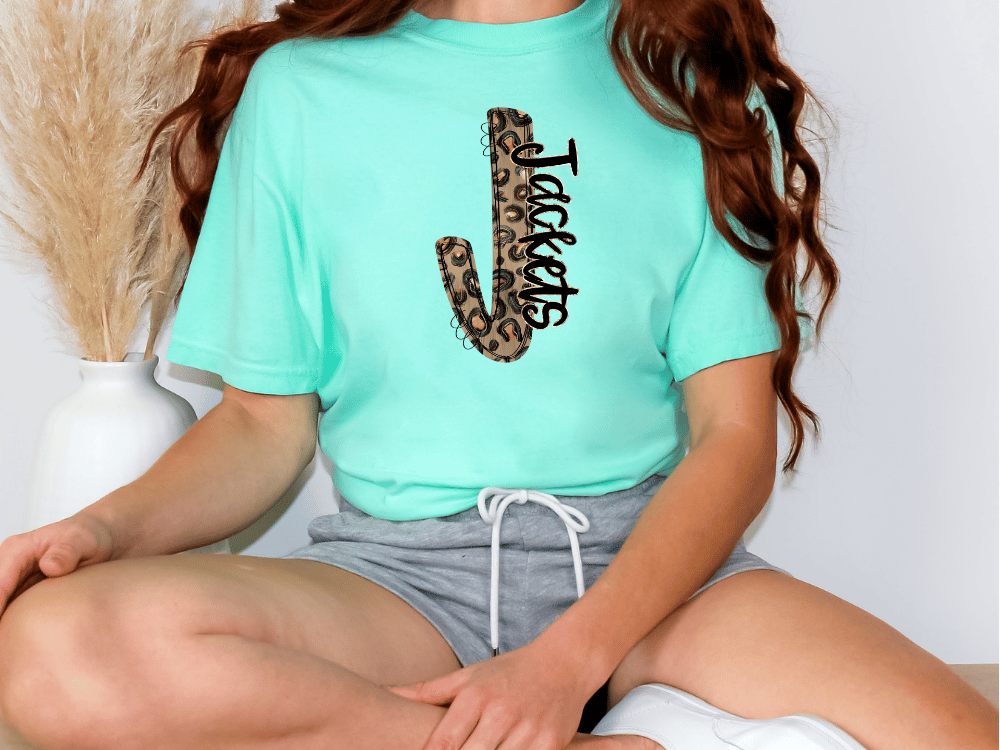 A person wearing a turquoise t-shirt with a leopard print design and gray shorts is sitting on the floor.