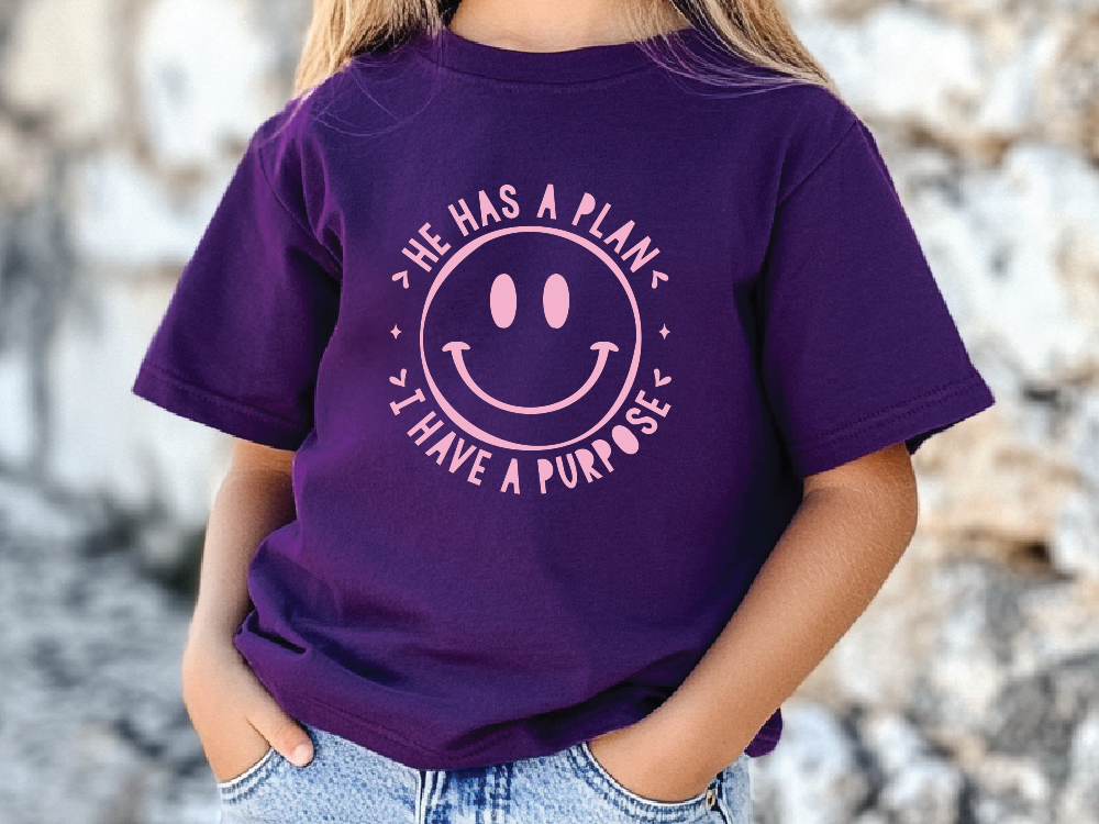 A person wearing a purple t-shirt with a smiley face design and text printed on it.