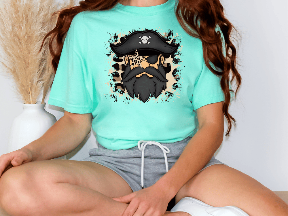 A person wearing a turquoise t-shirt with a pirate-themed graphic and gray shorts is sitting on the floor.