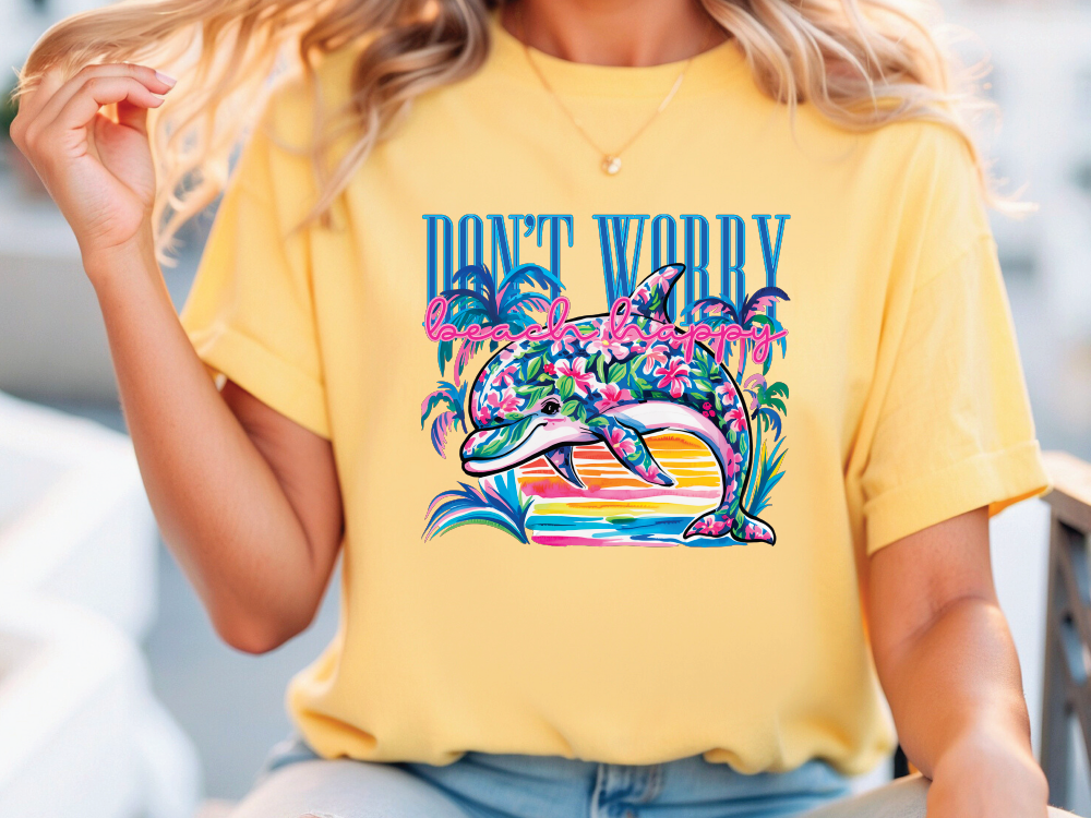 A woman wearing a yellow t-shirt with a colorful graphic of a dolphin and tropical plants printed on it.