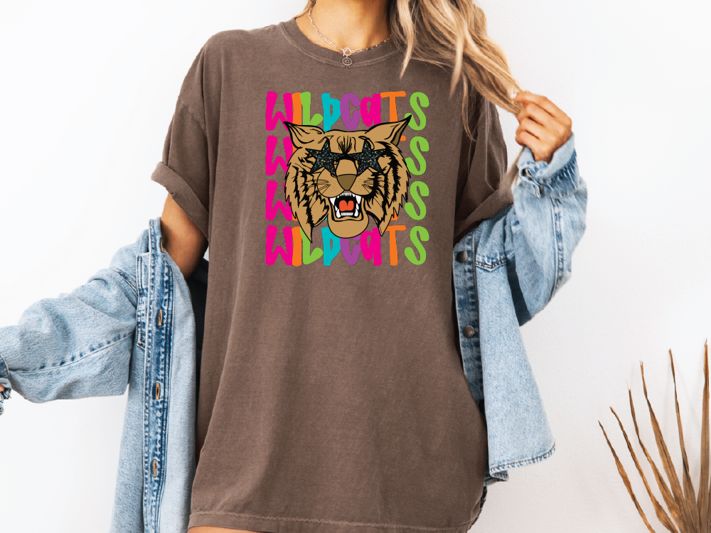 A woman wearing a brown t-shirt with a graphic of a tiger's face and the text "WILDCATS" printed on it.