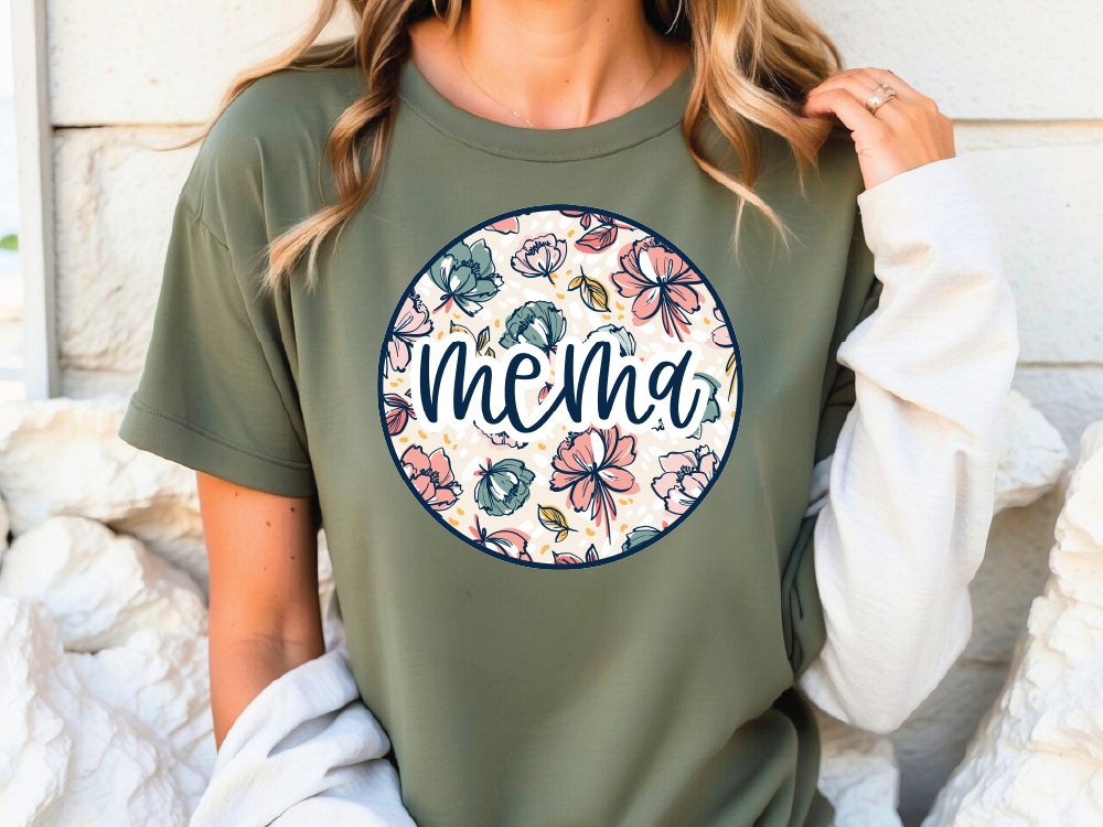 A woman wearing a green t-shirt with a floral design and the word "MEMA" printed on it.