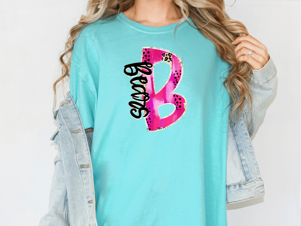 A woman wearing a turquoise t-shirt with a pink and black design on it, and a denim jacket.