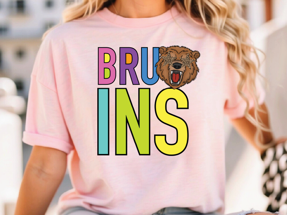 A woman wearing a pink t-shirt with the word "BRUINS" printed on it, featuring a graphic of a bear's head.
