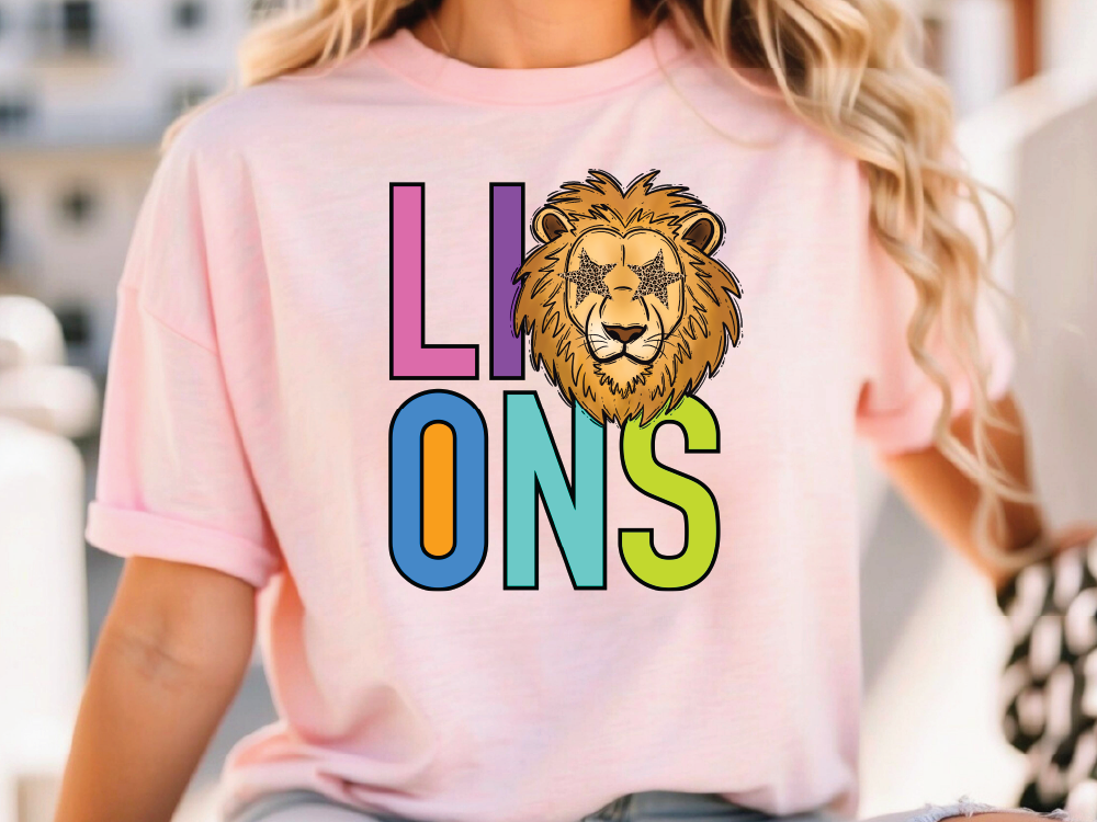 A woman wearing a pink t-shirt with a colorful graphic of a lion's head and the word "LIONS" printed on it.
