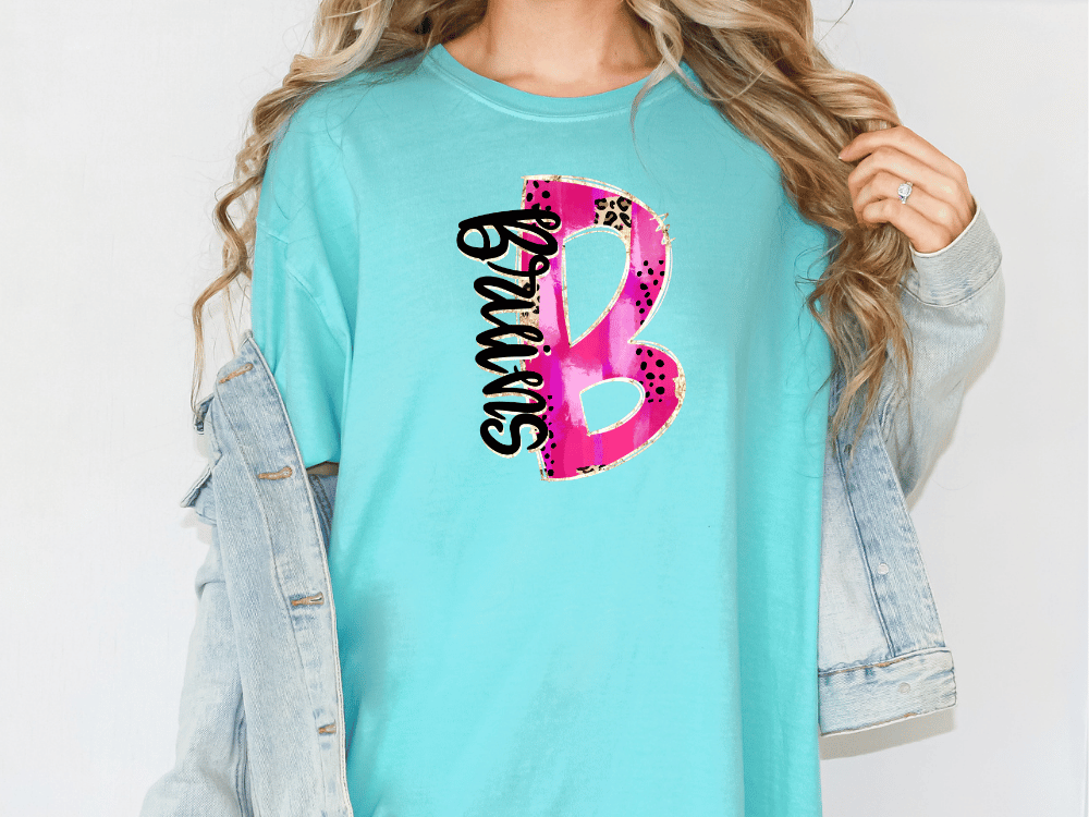 A woman wearing a turquoise t-shirt with a pink and black graphic design on it, standing against a white background.