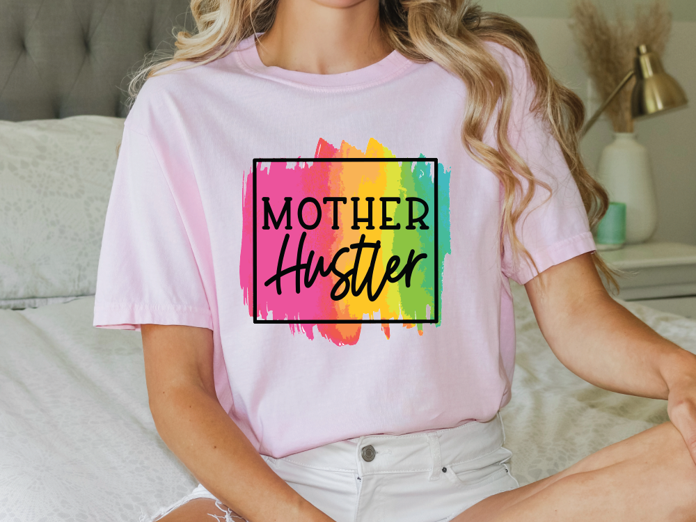 a woman sitting on a bed wearing a t - shirt that says mother huster