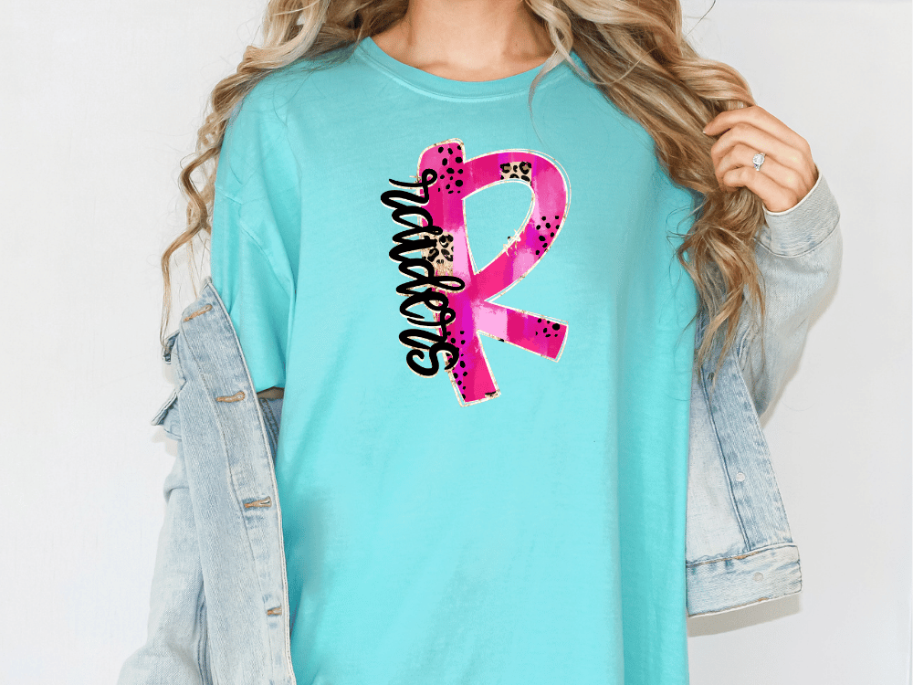 A woman wearing a turquoise t-shirt with a pink and black design on it, and a denim jacket.