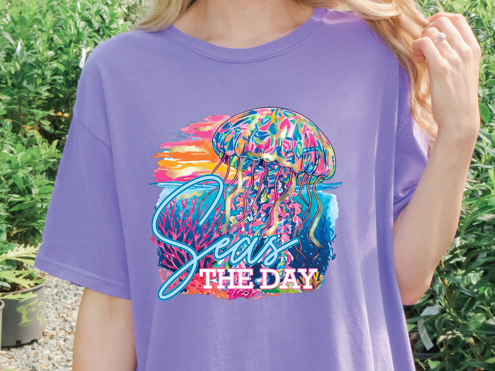 A person wearing a purple t-shirt with a colorful graphic of a jellyfish and the text "Seas the Day" printed on it.