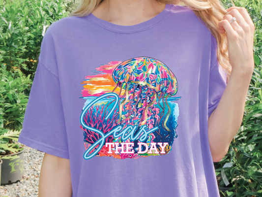 A person wearing a purple t-shirt with a colorful graphic of a jellyfish and the text "Seas the Day" printed on it.