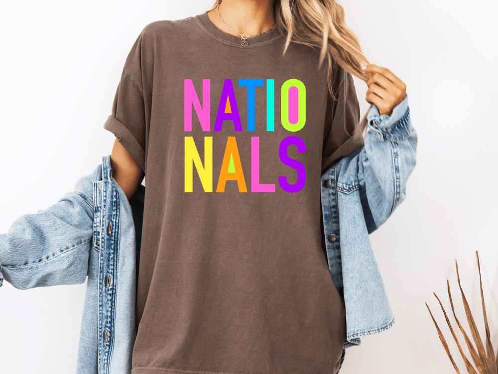 A person wearing a brown t-shirt with the text "NATIO NALS" in colorful letters, paired with a denim jacket.