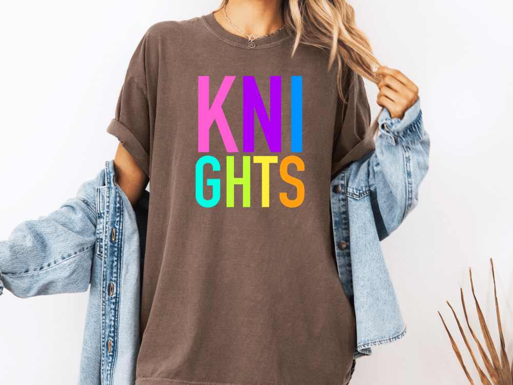 A person wearing a brown t-shirt with the text "KNIGHTS" in colorful letters, along with a denim jacket, stands against a white background.