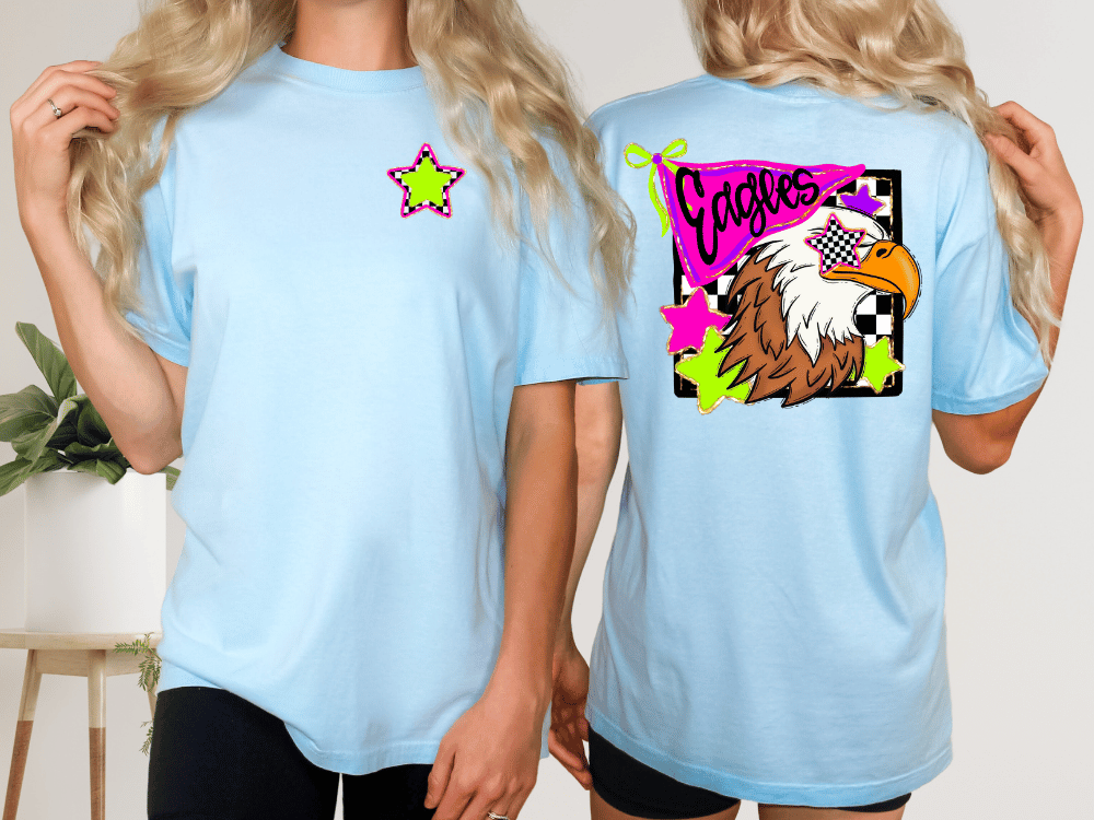 two women wearing light blue t-shirts with a graphic design featuring a stylized eagle and colorful elements.