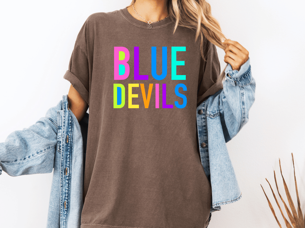 A person wearing a brown t-shirt with the text "BLUE DEVILS" printed on it, along with a denim jacket.