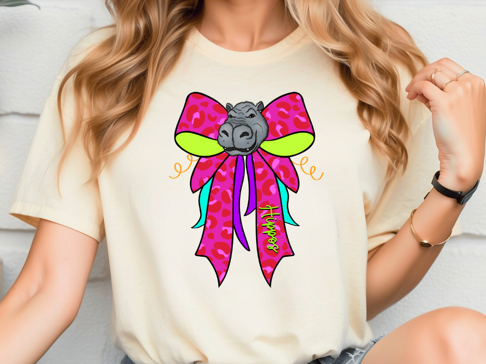 A woman wearing a white t-shirt with a colorful graphic design of a hippopotamus wearing a pink bow.