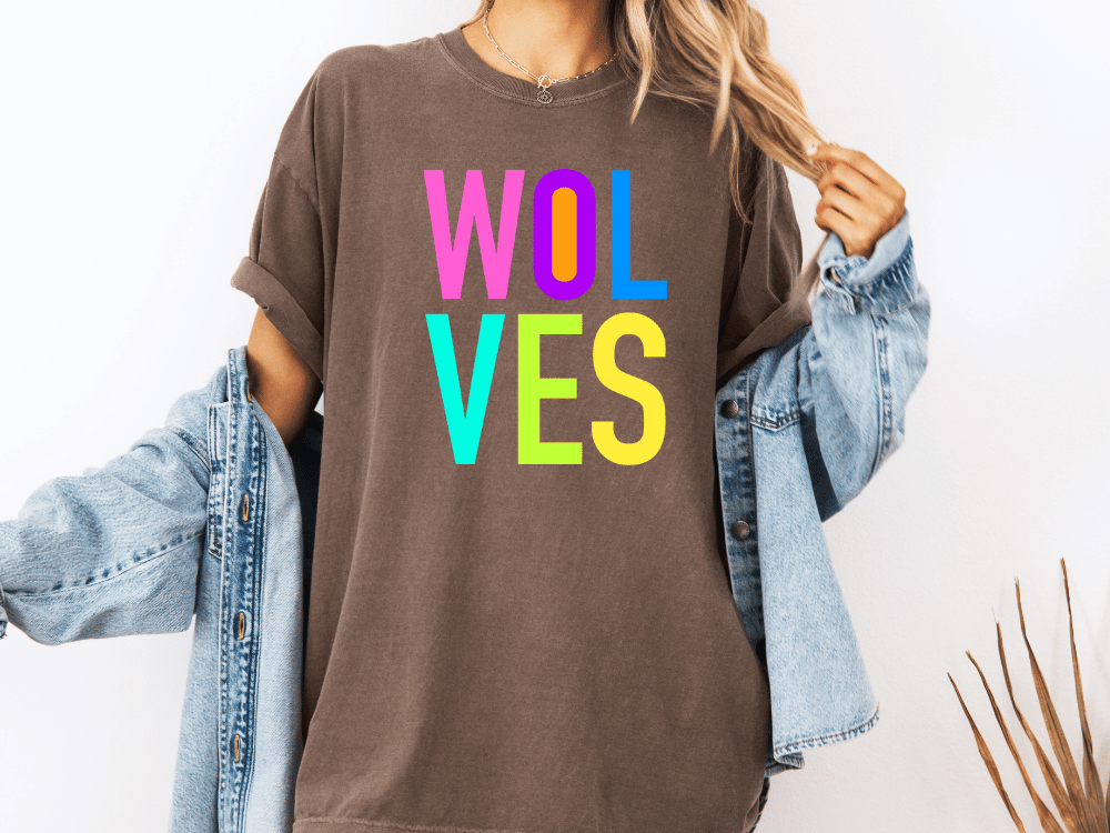 A person wearing a brown t-shirt with the text "WOLVES" in colorful letters, paired with a denim jacket, stands against a white background.