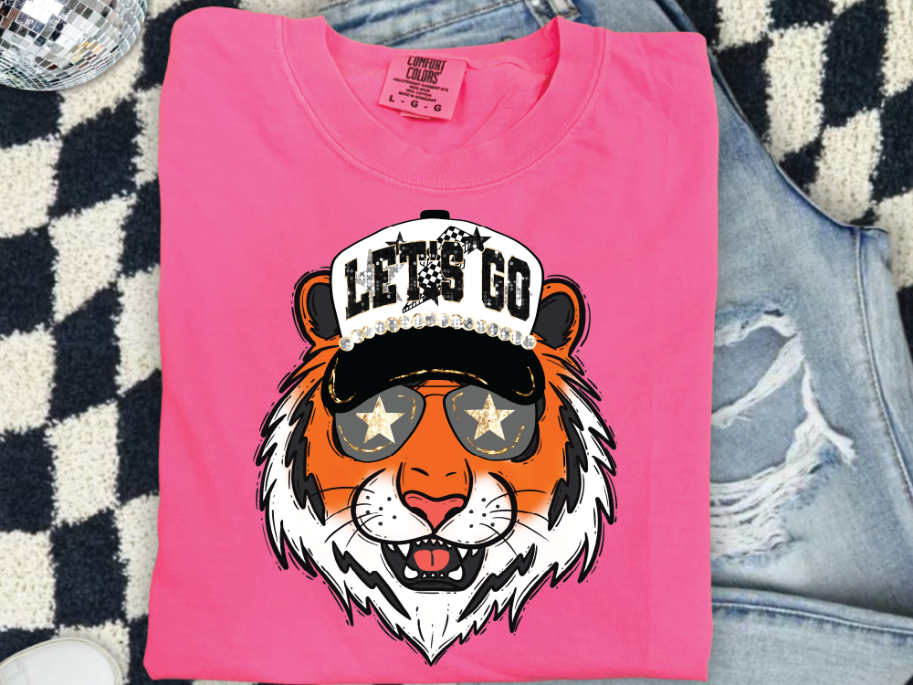 A pink t-shirt with a graphic design of a tiger wearing sunglasses and a hat with the text "LET'S GO" printed on it.