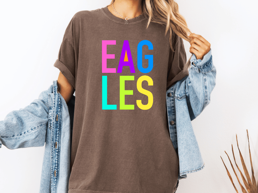 A person wearing a brown t-shirt with the word "EAGLES" printed in colorful letters.