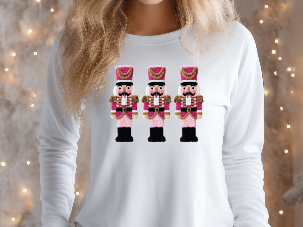 A woman wearing a white long-sleeved shirt with a design of three nutcracker men in pink and gold outfits.