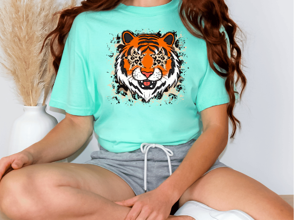A person wearing a turquoise t-shirt with a tiger graphic and gray shorts is sitting on the floor.