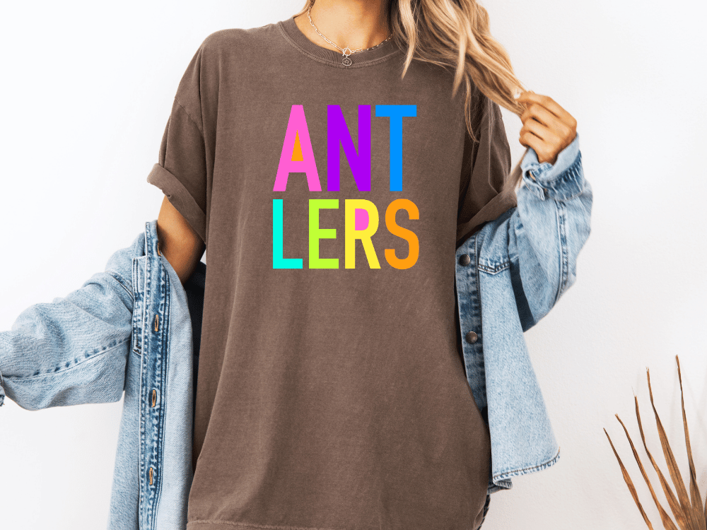 A person wearing a brown t-shirt with the text "ANT LERS" in colorful letters, paired with a denim jacket.
