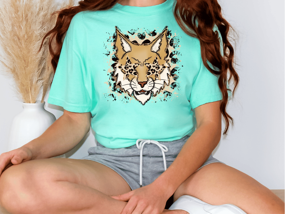 A person wearing a turquoise t-shirt with a graphic of a leopard on it, sitting cross-legged on the floor.