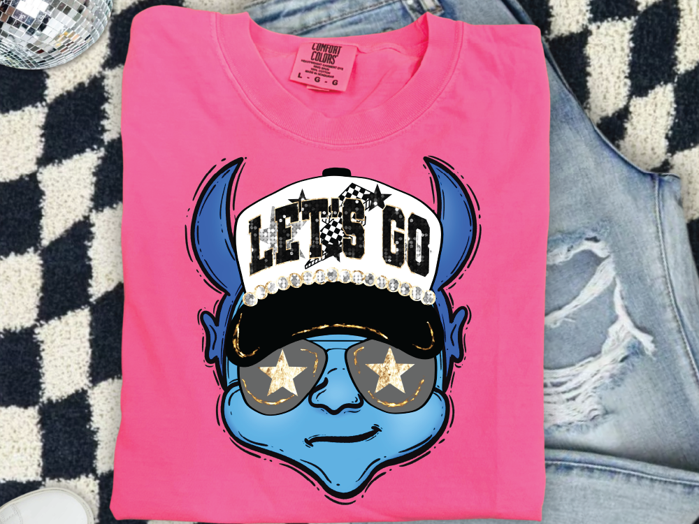 A pink t-shirt with a graphic design of a blue cartoon character wearing sunglasses and a hat with the text "LET'S GO" printed on it.