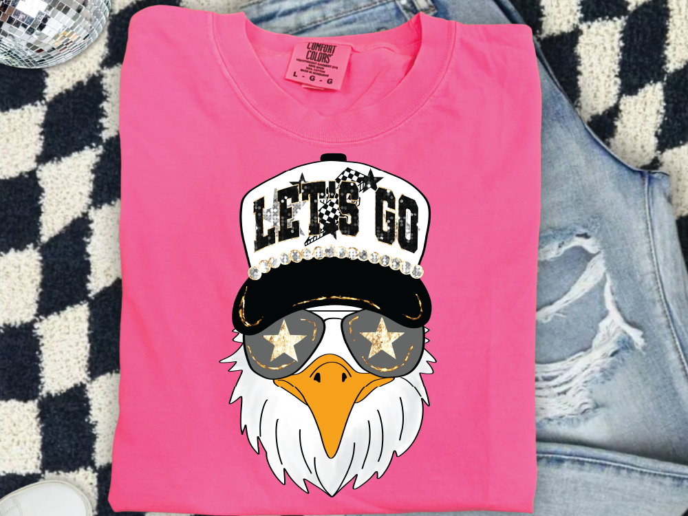 A pink t-shirt with a graphic of an eagle wearing sunglasses and a hat with the text "LET'S GO" printed on it.