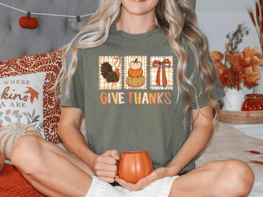 A woman sitting on a bed with a green t-shirt that says "Give Thanks" and holding a pumpkin-shaped mug.