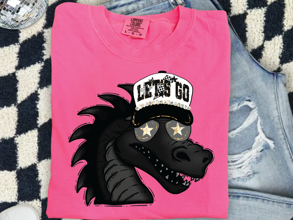 A pink t-shirt with a graphic of a cartoon dragon wearing a baseball cap and sunglasses, along with the text "LET'S GO".