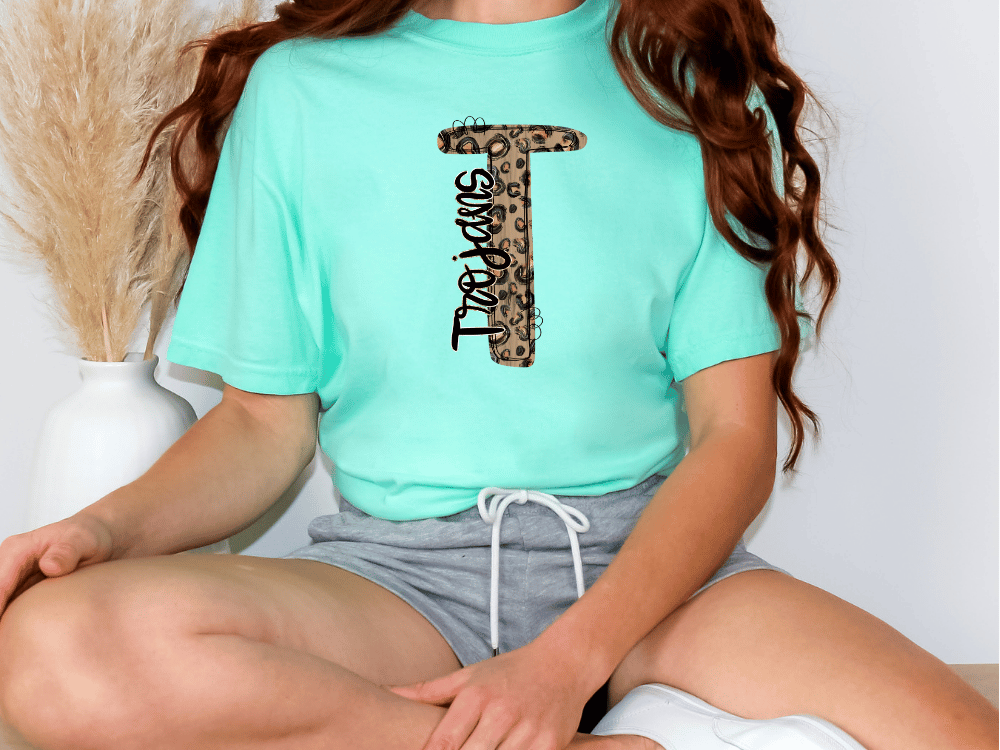 A person wearing a turquoise t-shirt with a leopard print design and gray shorts is sitting on the floor.