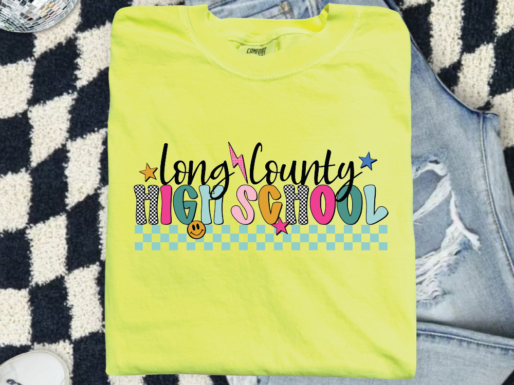 A bright yellow t-shirt with colorful text and graphics, including a smiley face, stars, and checkered patterns, is displayed on a patterned surface.