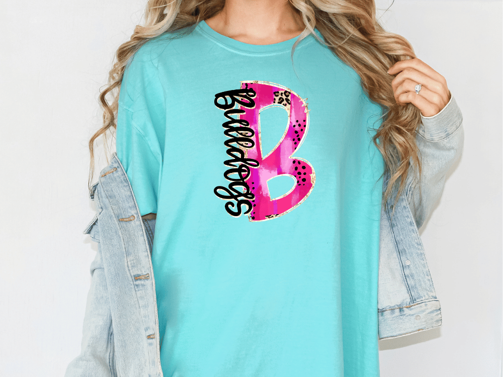 A woman wearing a turquoise t-shirt with a pink and black graphic design on it, along with a denim jacket.