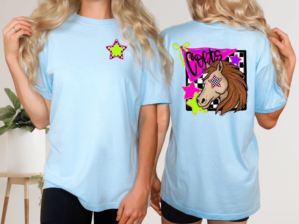 two women wearing light blue t-shirts with colorful designs. The t-shirt on the left has a star and a graphic of a unicorn, while the t-shirt on the right features a graphic of a horse with a checkered pattern and the word "Corns" written on it.