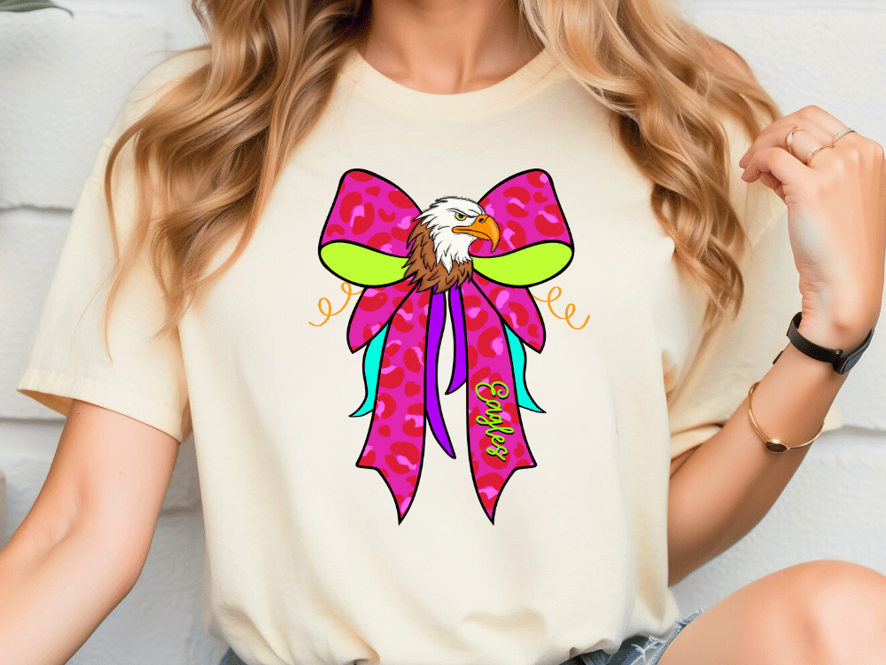 A woman wearing a white t-shirt with a colorful graphic design of an eagle wearing a pink bow.