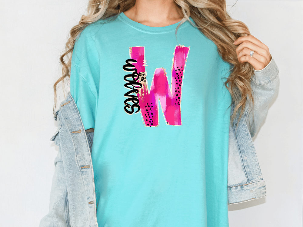 A woman wearing a turquoise t-shirt with a pink and black graphic design on it, and a denim jacket.