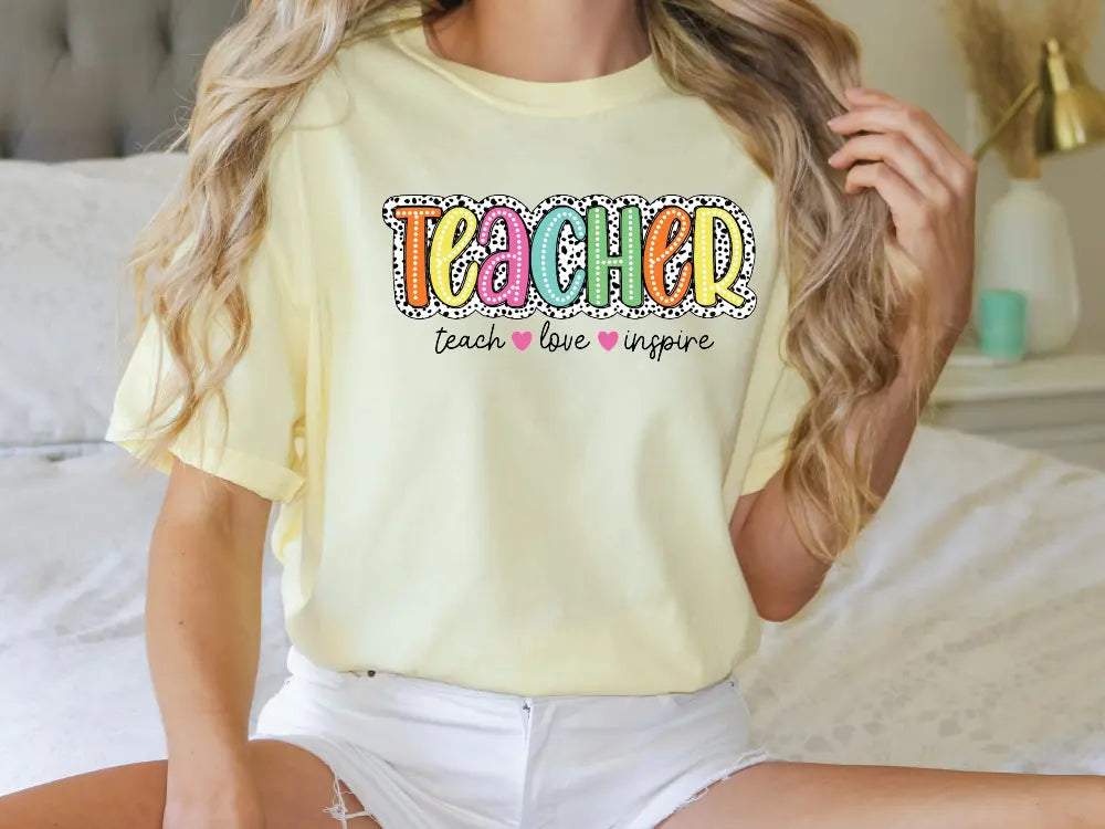 a woman sitting on a bed wearing a yellow teacher shirt