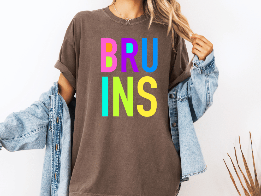 A person wearing a brown t-shirt with the word "BRU INS" in colorful letters, paired with a denim jacket.