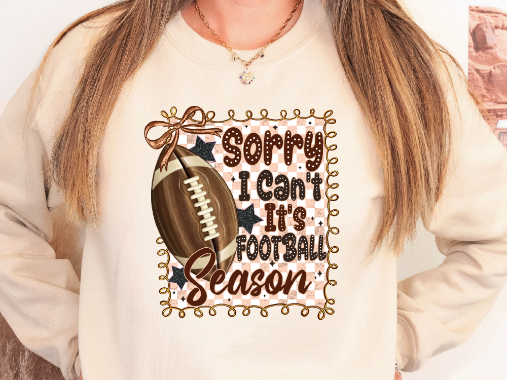 A person wearing a white sweatshirt with a graphic design featuring a football and the text "Sorry I Can't It's Football Season" printed on it.