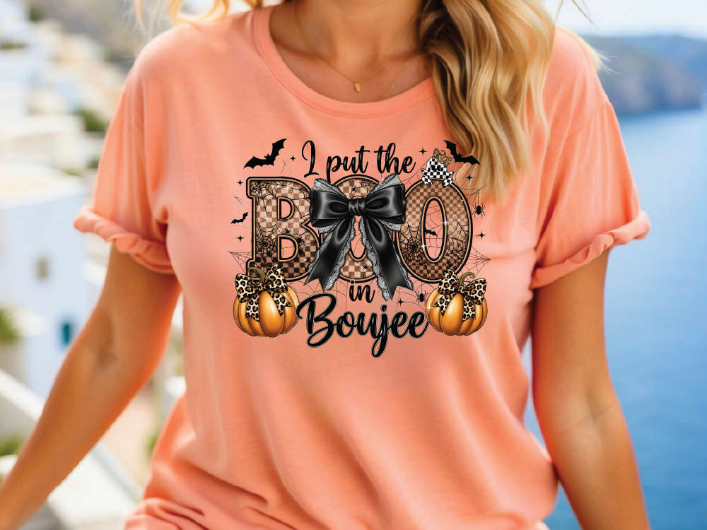 A woman wearing a pink t-shirt with a graphic design featuring a bow, pumpkins, and text that says "I put the BOO in BOUJEE".