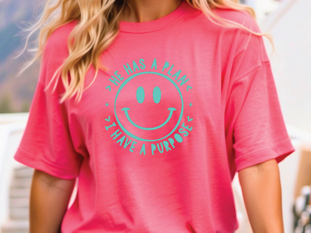 A person wearing a pink t-shirt with a smiley face design and text printed on it.