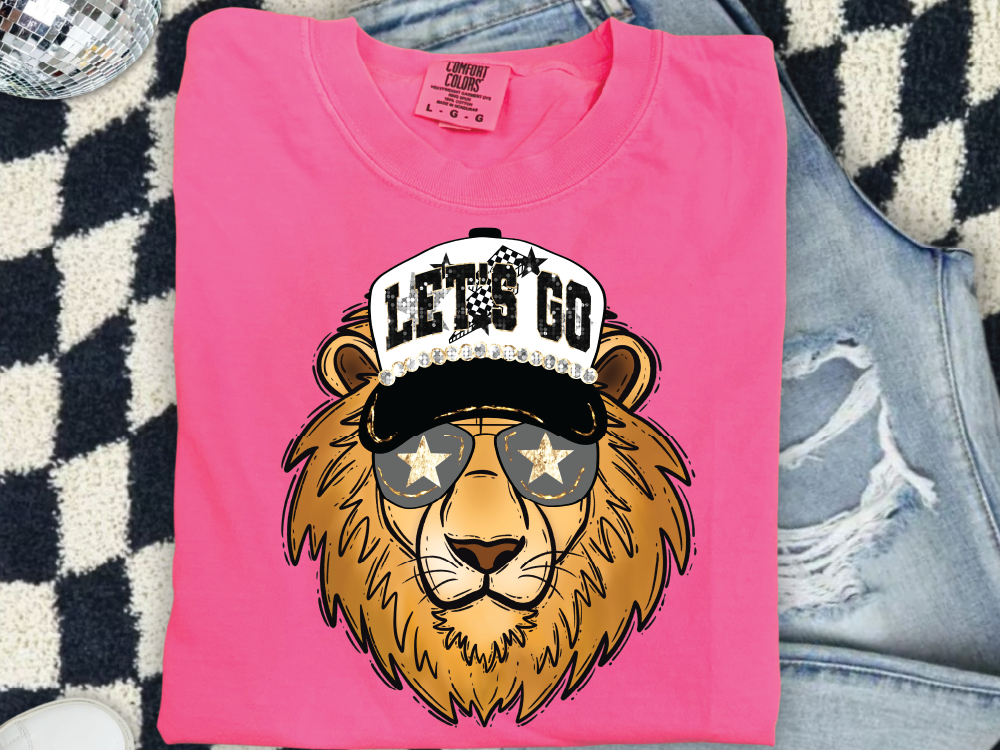 A pink t-shirt with a cartoon lion wearing sunglasses and a baseball cap with the text "LET'S GO" printed on it.