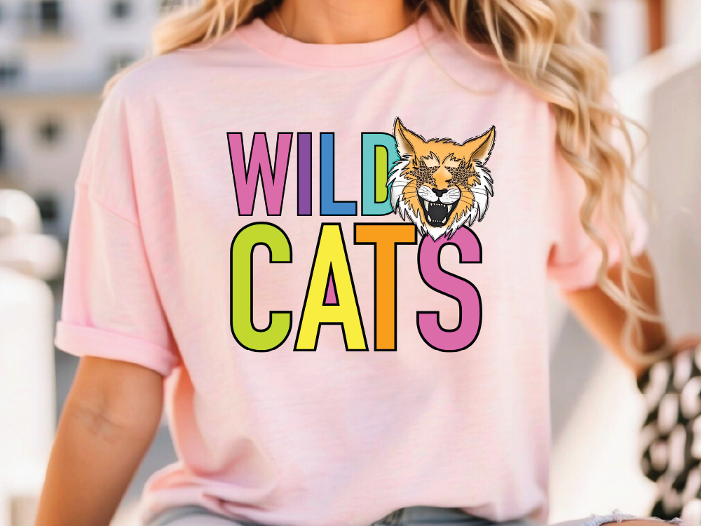 A woman wearing a pink t-shirt with the text "WILD CATS" printed on it.